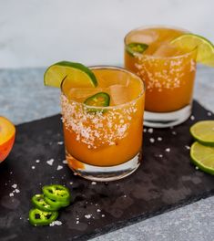 two glasses filled with drinks sitting on top of a cutting board next to sliced fruit