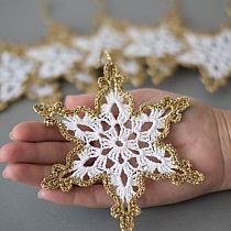 a hand holding a gold and white crochet snowflake ornament