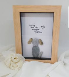 a stuffed animal in a wooden frame on a white blanket next to a small flower