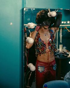 a woman with black makeup and red pants in front of a mirror wearing beaded clothing