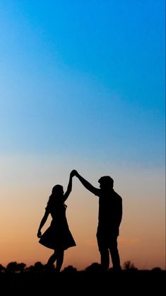 the silhouette of two people holding hands in front of an orange and blue sky at sunset