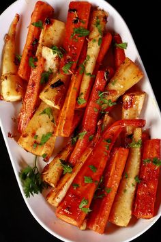 cooked carrots with sauce and parsley in a white dish on a black surface