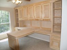 an empty room with wooden cabinets and a desk in the corner, next to a window