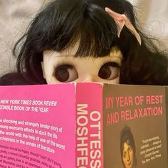 a doll with long black hair is holding a book in front of her face and looking at the camera