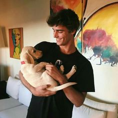 a man holding two puppies in his arms and smiling at the camera while standing next to a couch