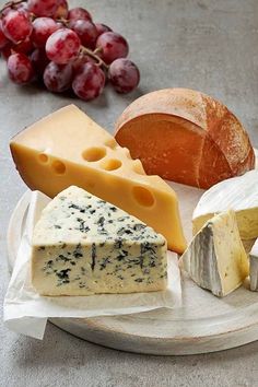 various types of cheese on a plate with grapes and bread