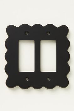 two black scalloped switchplates on a white wall, with one facing the camera