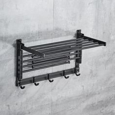 a black metal shelf with four hooks on it and a wall mounted towel rack in the background