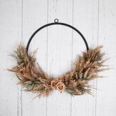 a wreath with dried flowers and leaves hanging on a white wooden wall in the shape of a circle