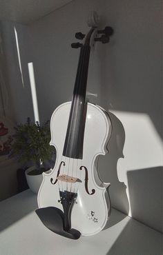 a white violin sitting on top of a table next to a potted plant in a window sill