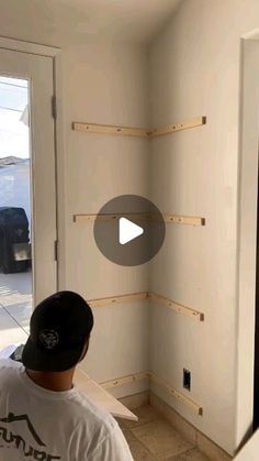 a man is working on the wall in his house with wood shelves and white walls