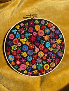 an embroidery project with colorful flowers on a yellow fabric background, in the shape of a circle