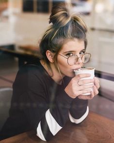 a woman sitting at a table drinking from a cup