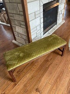 a green bench sitting on top of a hard wood floor next to a fire place