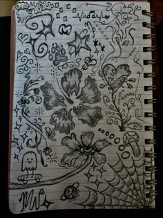 a notebook covered in doodles and flowers on top of a wooden table next to a pen