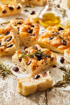 bread with olives, rosemary and oil on a white tablecloth surrounded by other food items