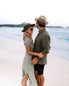 a man and woman are standing on the beach with their arms around each other as they hug