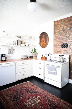 an old fashioned kitchen with white appliances and red rug on the floor in front of brick wall