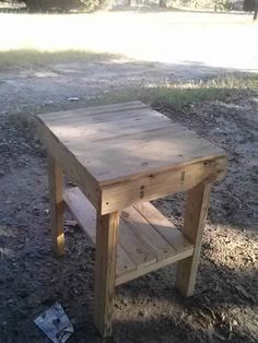 a small wooden table sitting in the middle of a dirt field next to a tree