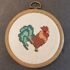 a cross stitch pattern with a chicken and rooster on it's back, in a wooden frame