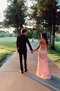 a man and woman holding hands walking down a sidewalk