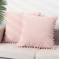 two pink pillows sitting on top of a couch next to a potted palm tree