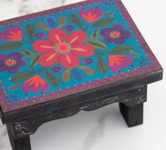 an artistically painted wooden stool with flowers on the top and bottom, sitting on a marble surface