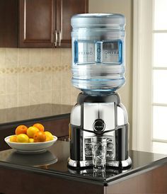 a water dispenser sitting on top of a counter next to a bowl of fruit