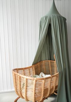 a wicker bed with a canopy in front of a white wall and wooden floor