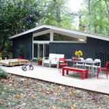 a patio with chairs, tables and a bike parked in front of the house that is surrounded by trees