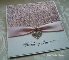 a wedding card with a pink ribbon and a heart brooch hanging from the front