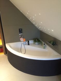 a bathroom with a white bath tub sitting under a slanted ceiling next to a plant