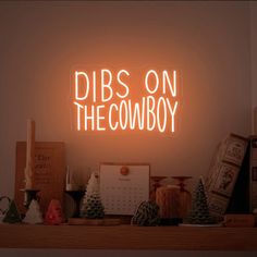 a neon sign that says dibs on the cowboy in front of some christmas decorations