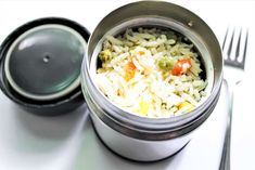 a close up of a container with rice and carrots on the side next to a fork