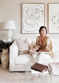 a woman sitting on a white couch in front of two paintings and a coffee table