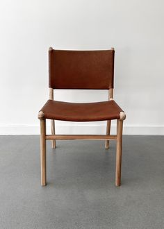 a brown leather chair sitting on top of a cement floor next to a white wall