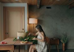 a woman sitting at a table with food in front of her on the floor next to a lamp