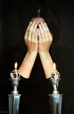 a woman covering her face next to two candles with both hands on top of them