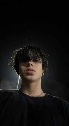 a young man with dark hair standing in the dark