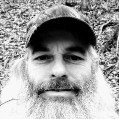 a black and white photo of a man with a long beard wearing a baseball cap