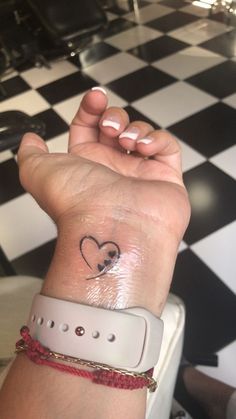 a woman's wrist with a small heart tattoo on her left hand and a black and white checkered floor