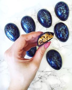 a hand is holding an egg shell filled with blue speckles on a marble surface