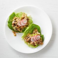 two lettuce leaves with radishes and nuts on them sitting on a white plate