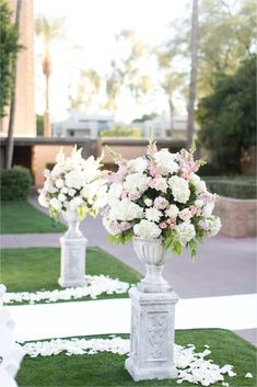 white vases with pink and white flowers are lined up on the grass in front of a building