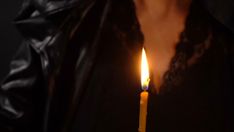 a woman holding a lit candle in her right hand and wearing a black leather jacket