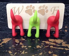 three dog shaped magnets sitting on top of a wooden sign with paw prints in red, green and blue