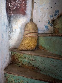 a broom sitting on top of a set of steps next to a wall with peeling paint