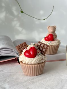 two cupcakes with chocolate and heart decorations on them next to an open book