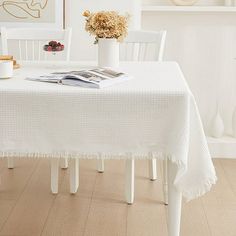 the table is covered with white linens and has flowers in a vase on it