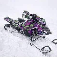 a purple and black snowmobile sitting in the snow with its skis on it's side